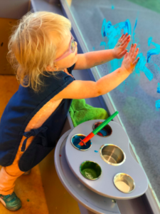 A young child is standing and hand painting on the wall with both hands. 